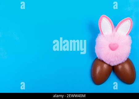 Easter, chocolate egg, pink toy rabbit head on a blue background. Place for text Stock Photo