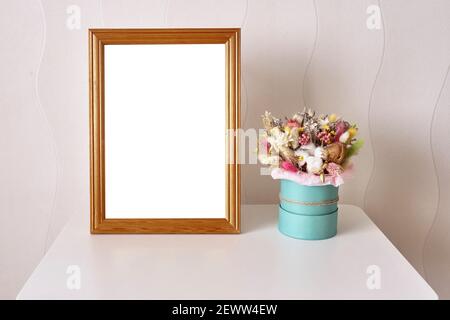 A picture in a wooden frame and a beautiful bouquet of dried flowers on the white table. Interior composition. Mockup Stock Photo