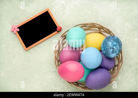 empty chalkboard and colorful easter eggs in a basket on green background Stock Photo