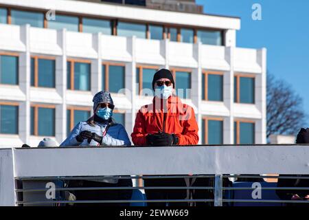 Face mask wearing couple on Suomenlinna ferry deck with former Enso-Gutzeit headquarters in the background in Helsinki, Finland Stock Photo