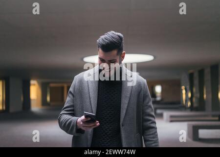 Young businessman sending a message with his cell phone while smiling. Stock Photo