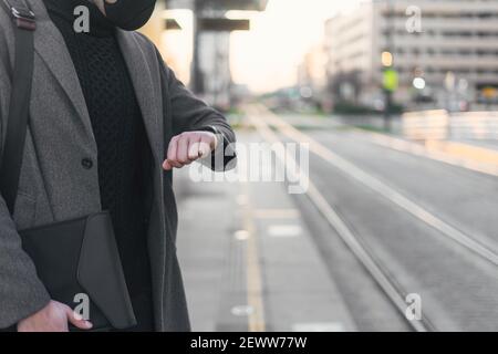 Unrecognizable businessman in face mask waiting for train looking at his watch. Stock Photo