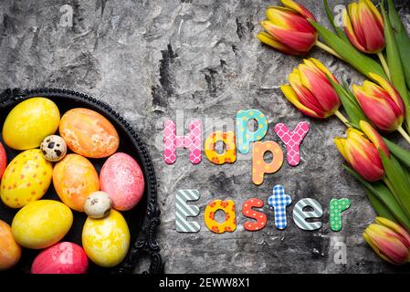 Happy Easter card with colorful red and yellow tulips with hand painted Easter eggs on a wooden table tabletop view with copy space Stock Photo