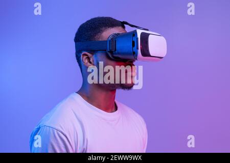 Black Man In VR Headset Standing In Neon Light Over Purple Background Stock Photo