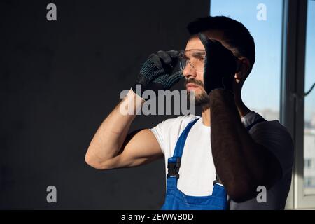 Repairman in blue overalls putting on safety glasses Stock Photo