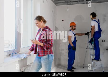 A customer stands by the window and examines documents, foremen in the background are working Stock Photo