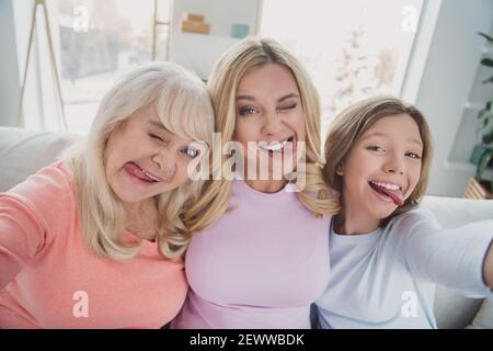 Photo portrait of different generations women taking selfie grimacing fooling showing tongues at home silly faces Stock Photo