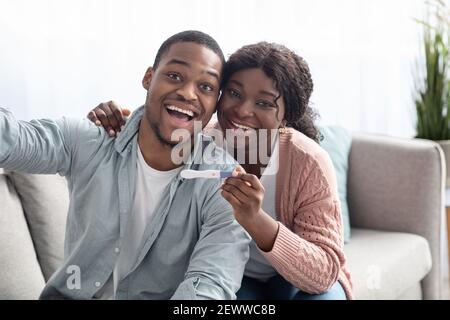 Happy black couple with positive pregnancy test taking selfie Stock Photo