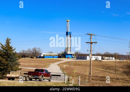 Drilling Rig and site for large oil-gas well with buildings and equipment - red truck with trailer at closed gate leading down to it Stock Photo