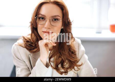 Portrait of gorgeous redhead business woman in stylish formal wear and eyeglasses. Beautiful caucasian female manager looking directly at the camera, showing self confidence and success Stock Photo