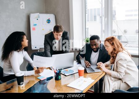 Meeting of business team. Group of successful people, are study financial graphs and diagrams, brainstorming together. Multiethnic employees discuss ideas, working on new project Stock Photo