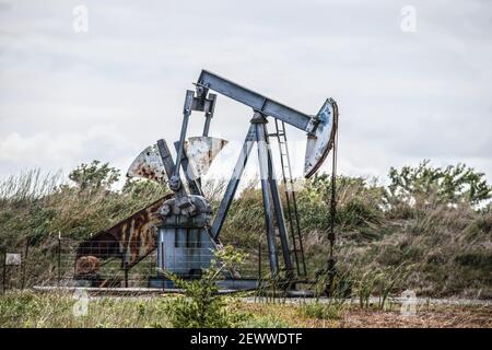 Working oil or gas well pump jack with windblown blurred weeds and scrub behind it - close-up Stock Photo