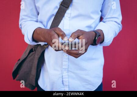 Midsection of african american man standing against red wall in the street using smartphone Stock Photo