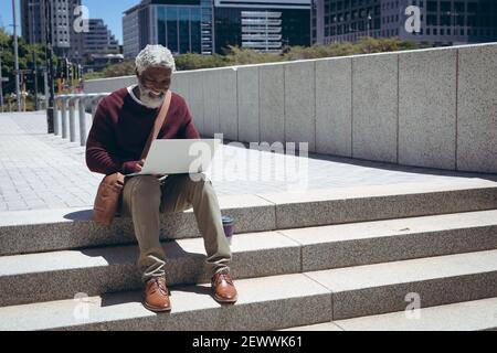 African american senior man sitting on steps in the street using laptop Stock Photo