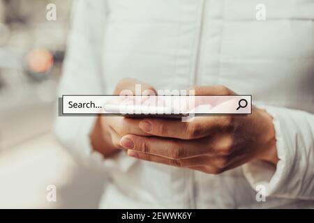 Internet search concept with a system and a magnifying glass on the background a girl holding a smartphone in her hands. Stock Photo