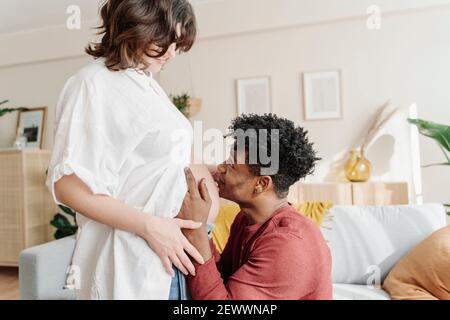 Tender black man kissing tummy of pregnant woman Stock Photo