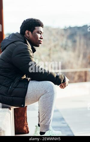 Portrait of an African American boy sitting on a bench in an urban space. Stock Photo
