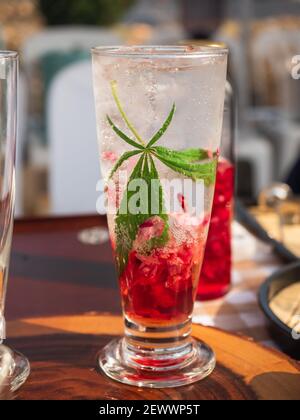 A glass of cold red Italian soda with marijuana or cannabis leaf Stock Photo