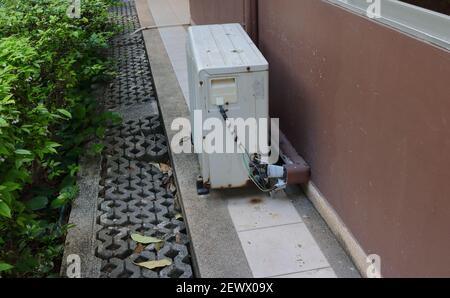 Connection of weathered electrical wires and refrigerant duct at rusty condensing unit outside a building Stock Photo