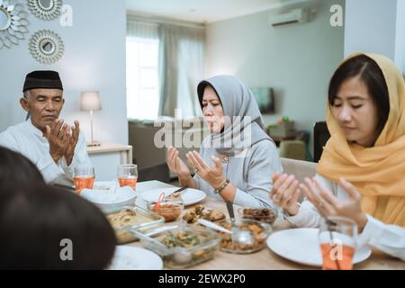 happy asian muslim family praying before having their iftar meal during ramadan fasting Stock Photo