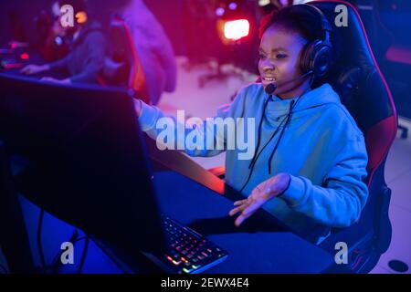 Streamer beautiful African girl regrets losing professional gamer loser playing online games computer, neon color. Stock Photo