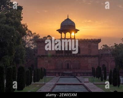 AGRA, INDIA - MARCH, 26, 2019: the sun rises behind a dome canopy on the naubat khana building in the gardens of the taj mahal Stock Photo