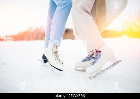 Closeup two women wearing white ice skates on winter sunset background. Stock Photo