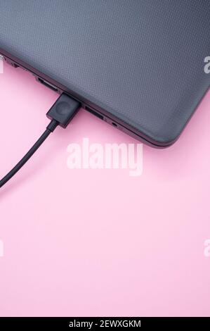 A vertical shot of a laptop with a charging cable isolated on an orange background Stock Photo