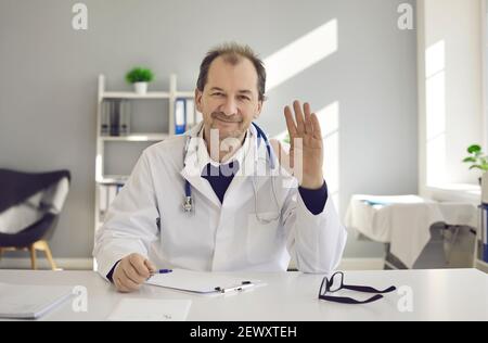 Friendly middle-aged doctor provides an online consultation to a patient via video link. Stock Photo