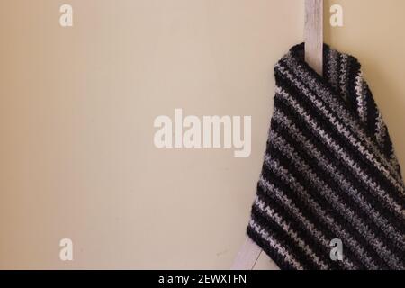 A classic black and white woolen muffler crocheted with the moss stitch pattern is kept on a stand with a yellow background. Copy space background. Stock Photo