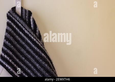 A classic black and white woolen muffler crocheted with the moss stitch pattern is kept on a stand with a yellow background. Copy space background. Stock Photo