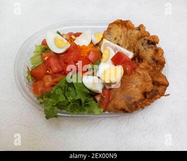 an overhead shot of delicious homemade fried meat schnitzels with salad of lettuce, tomato, hard boiled eggs and carrots in a tray. Takeaway Stock Photo