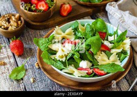 Italian pasta salad with strawberries, arugula, nuts, soft cheese dressed with balsamic sauce on the wooden table. Stock Photo
