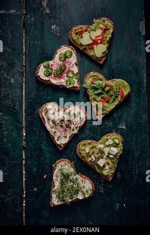 Top view of assorted heart shaped vegan toasts placed on dark rustic table Stock Photo