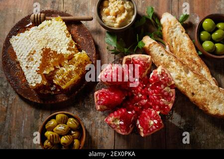 From above half of pomegranate and sweet honeycomb placed on wooden rustic table near olives and baguette toast with hummus Stock Photo