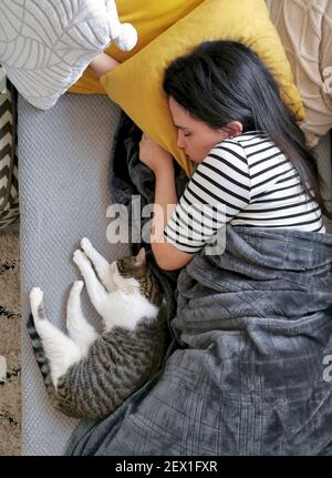 A young Caucasian woman sleeping on a couch with a cat under a warm blanket Stock Photo