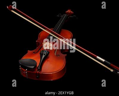 An old rustic child's violin with a bow on it, in black background Stock Photo