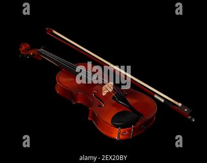 An old rustic child's violin with a bow in the side in black background Stock Photo
