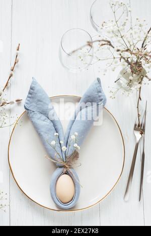 Table setting with egg in blue Easter Bunny napkin on golden rim plate. Top view. Stock Photo