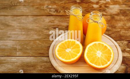 Fresh orange juice on wooden table on a wooden board. Sliced oranges and two bottles of juice Stock Photo