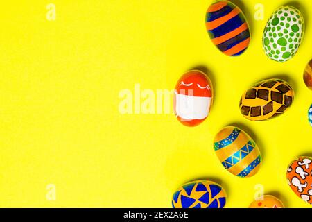 Colored colored eggs on a yellow background. One egg in a mask due to the quarantine of the covid-19 coronavirus. With a place for text to copy space Stock Photo