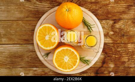 Fresh orange juice on wooden table on a wooden board. Sliced oranges and two bottles of juice. View from above. Rosemary sprigs for decoration Stock Photo