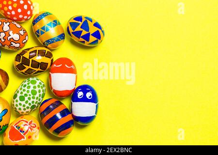 Colored colored eggs on a yellow background. Two eggs in a mask due to the quarantine of the covid-19 coronavirus. With a place for text copy space Stock Photo