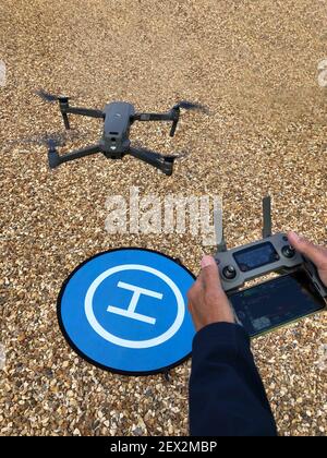 Operator with control and drone in flight with landing pad Stock Photo