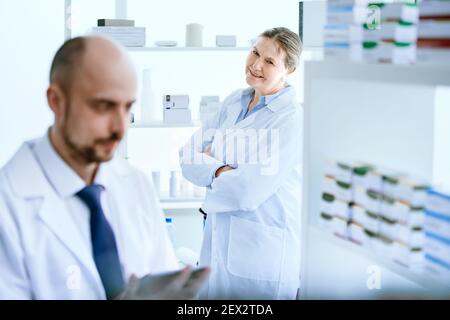 female pharmacist looking at a colleague with a digital tablet. Stock Photo