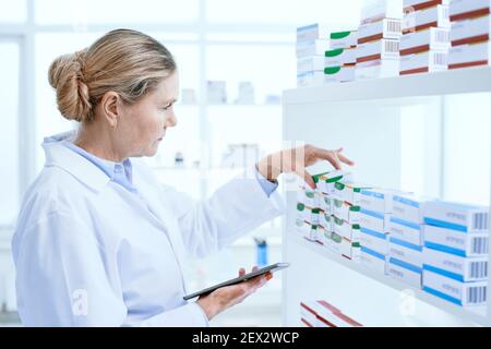 serious female pharmacist using a digital tablet in the workplace. Stock Photo