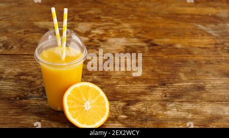 Orange juice in fast food closed cup with tubes on wooden table. Fresh summer drink. Photo for banner or advertisement of cafe and menu Stock Photo