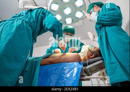 Asian surgeons team in surgical gown performing surgery a seriously injured patient in operating room at hospital Stock Photo