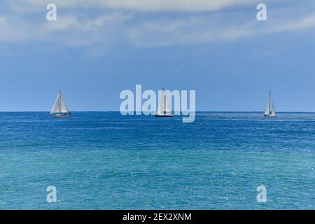 Three sailboats in a row on clear aqua teal blue ocean with clear sky and calm sea, evenly spaced and symmetrical, very tranquil and beautiful Stock Photo