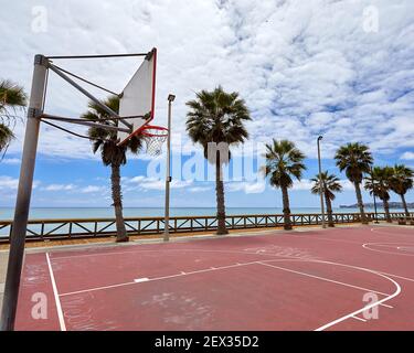 Outdoor street basketball court on beach in San Clemente California with orange surface and palm trees in the background showing hoop and backboard Stock Photo